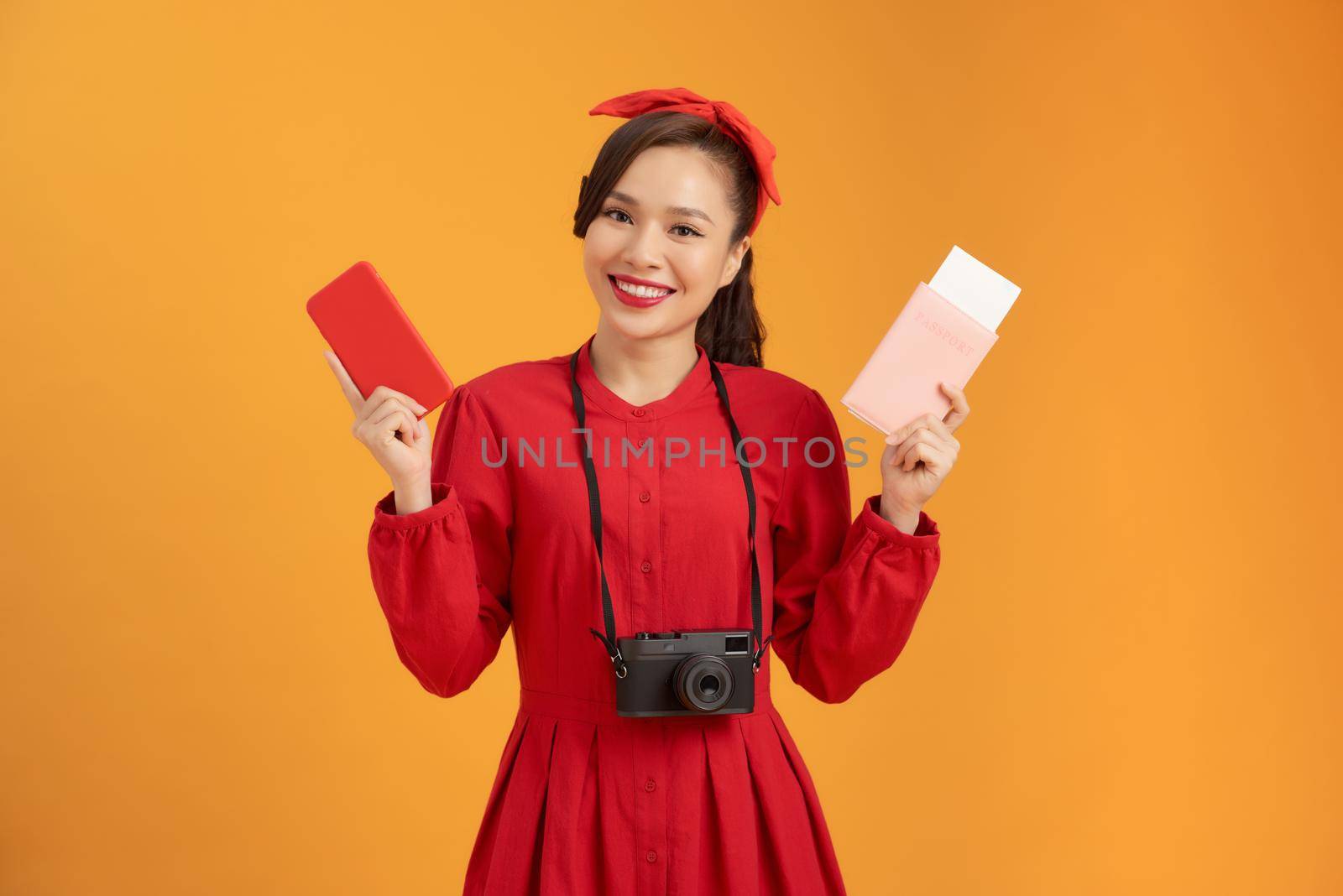 Happy tourist woman in summer red dress holding passport isolated on orange background.