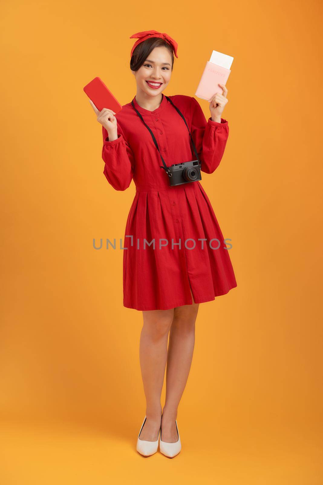 Happy tourist woman in summer red dress holding passport isolated on orange background. by makidotvn