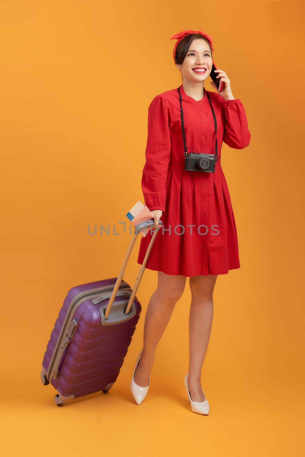 Young Asian woman bring suitcase and using phone isolated over orange background.