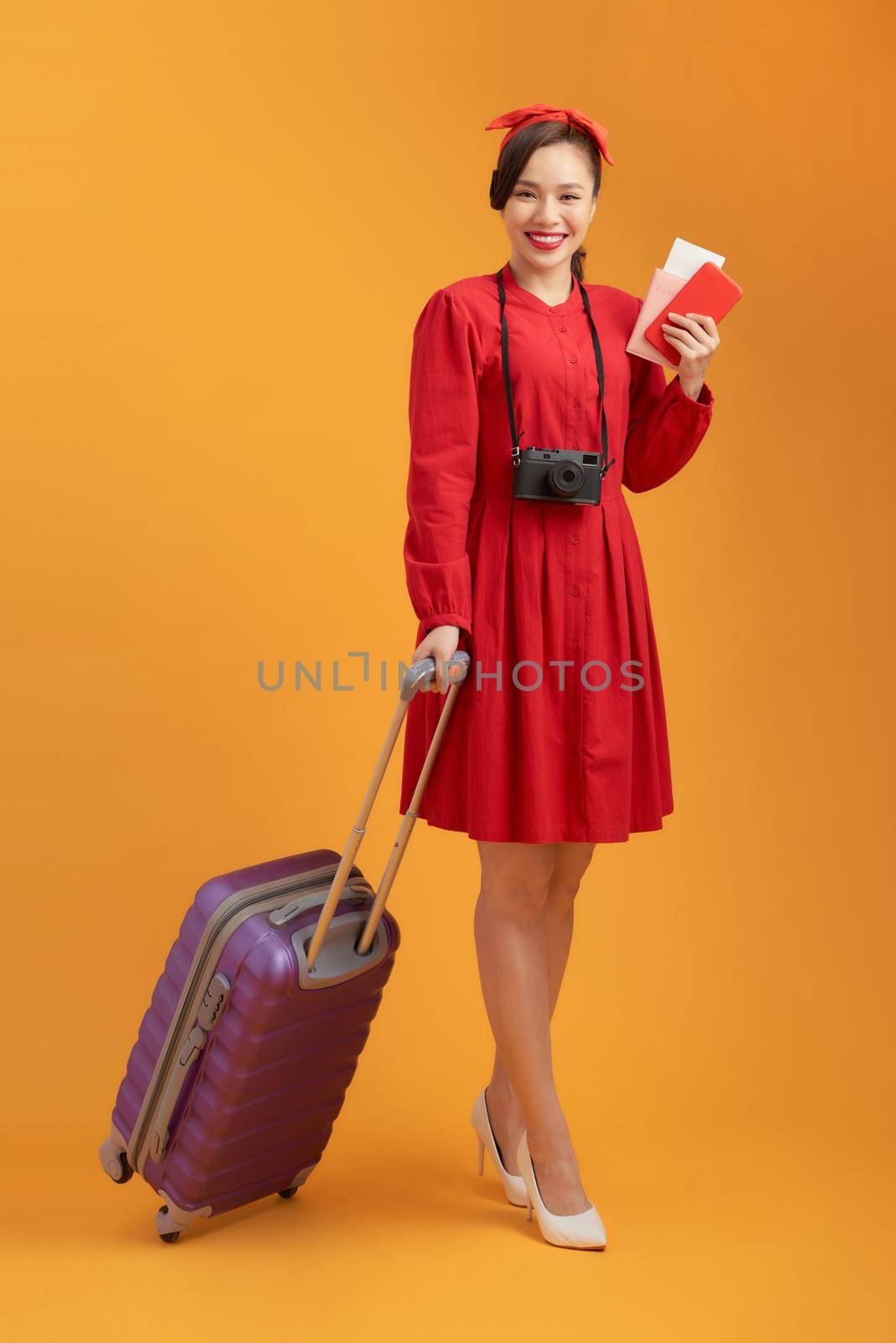 concept of travel. happy woman girl with suitcase, camera and passport on orange colored background by makidotvn