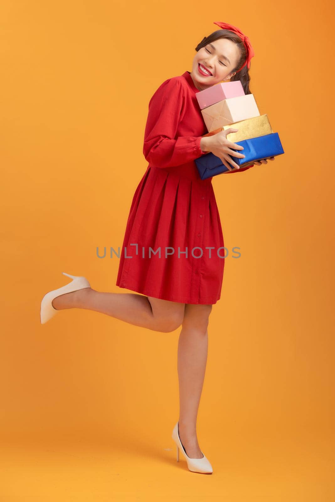 Smiling young Asian lady holding gift boxes isolated over orange background.