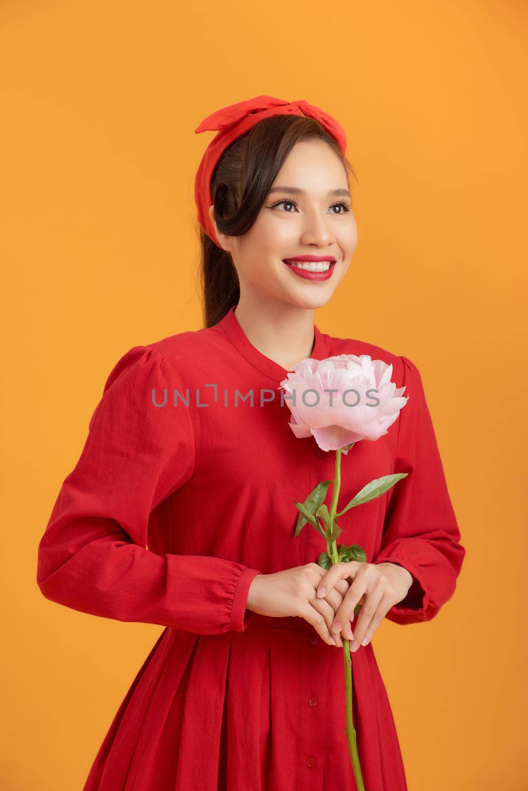 Close up young Asian woman holding peony flower over orange background. by makidotvn