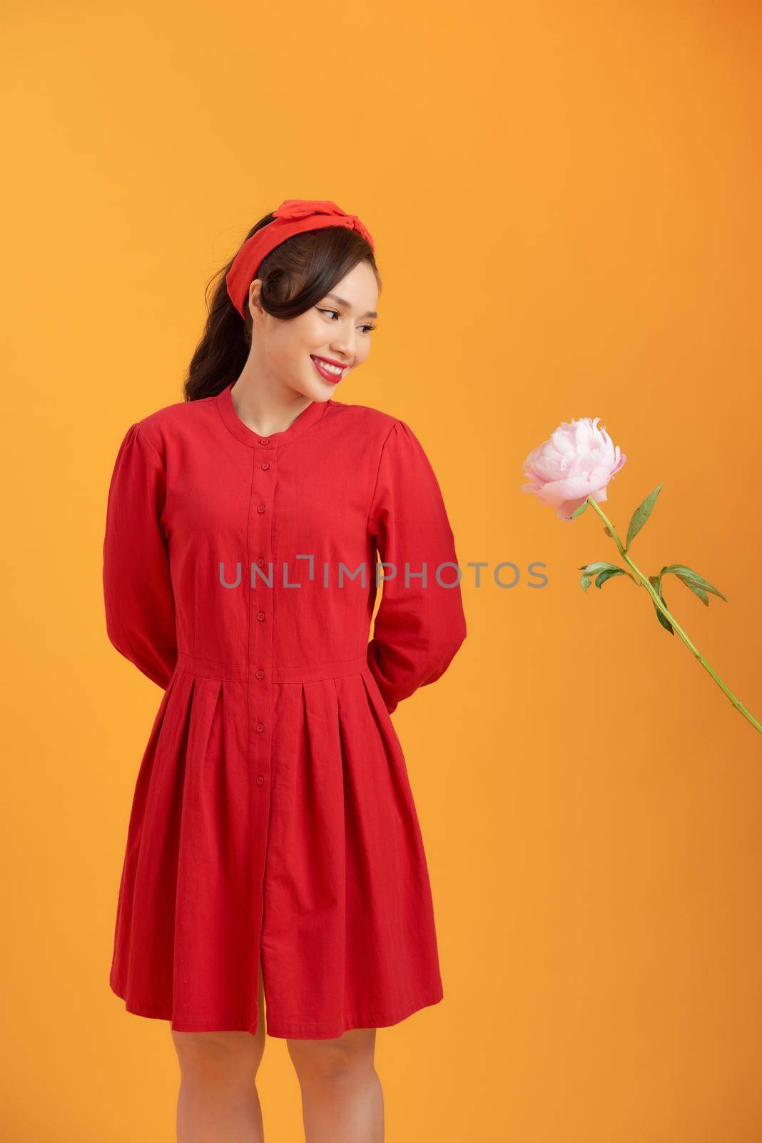 Charming young Asian in red dress holding peony flower isolated over orange background. by makidotvn