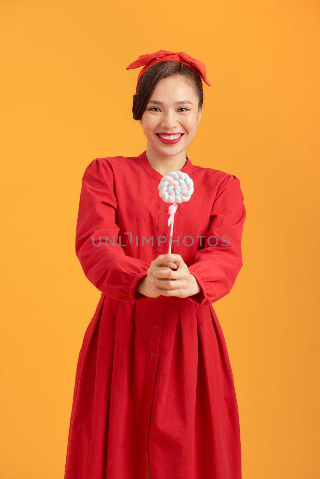portrait of a happy smiling woman holding lollipop and posing isolated on the orange background
