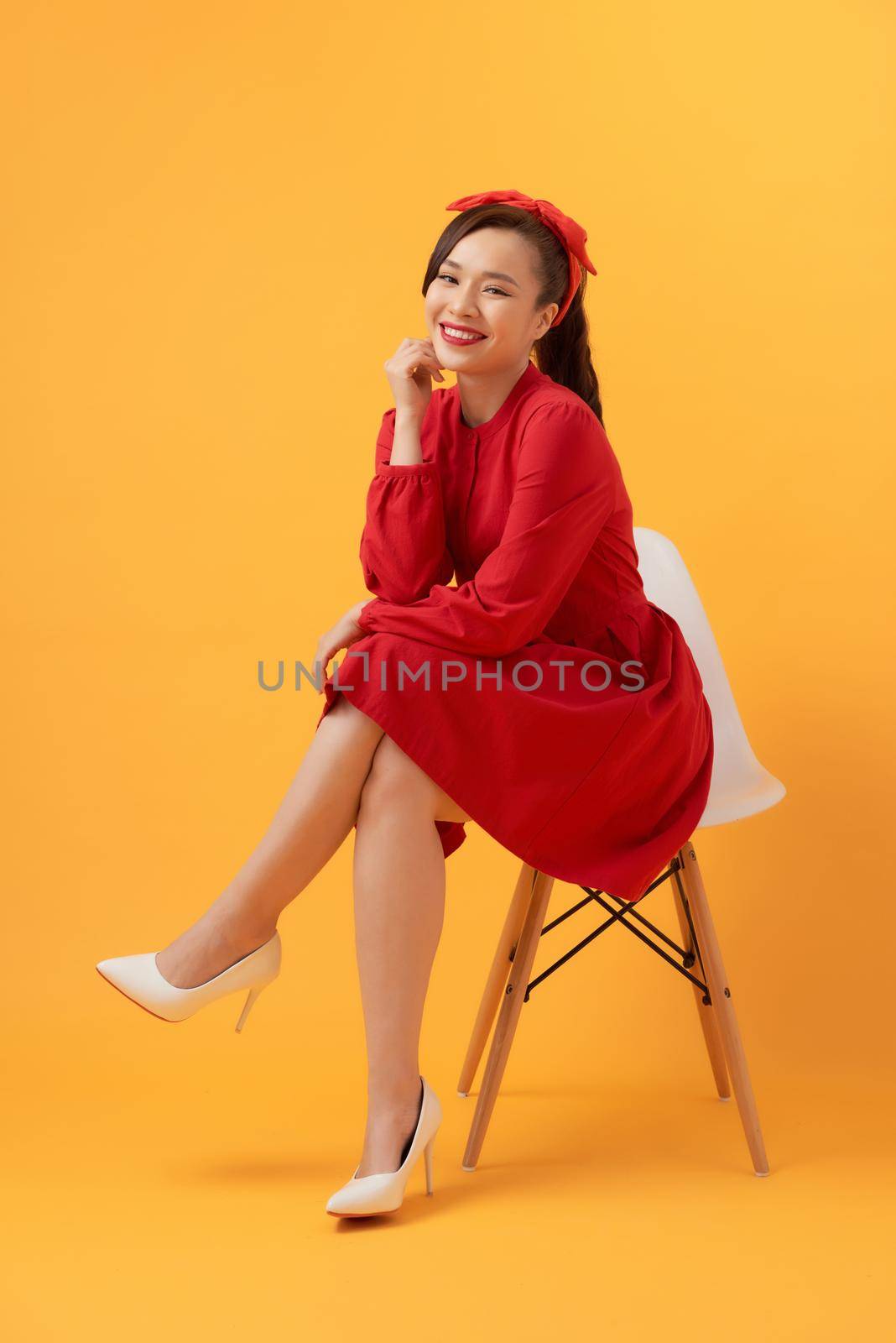 Young woman sitting in armchair on orange background