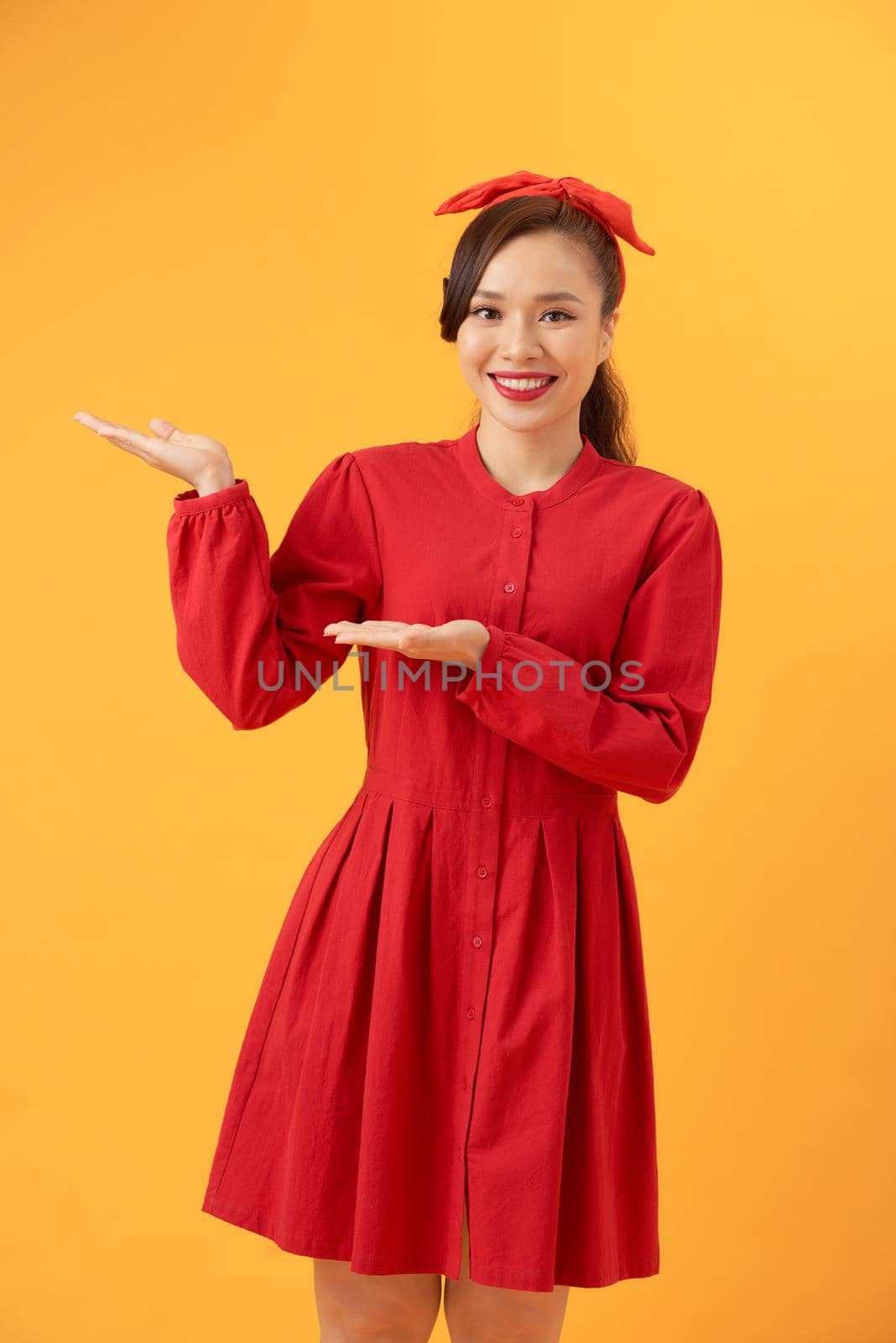Young Asian Woman in red dress pointing to copy space, isolated on orange background by makidotvn