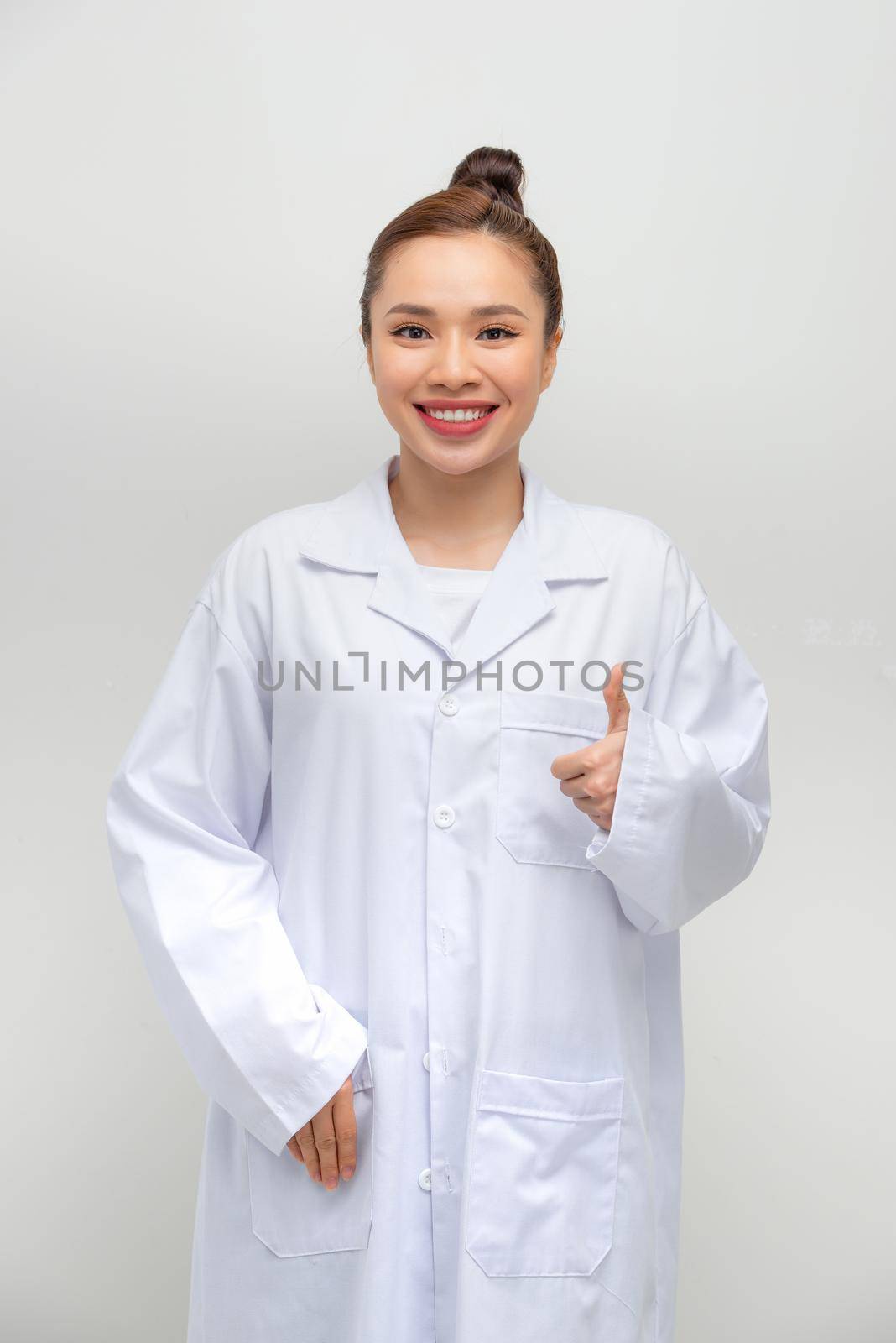 Happy, pretty, attractive, medic worker in white coat showing thumb up to the camera by makidotvn
