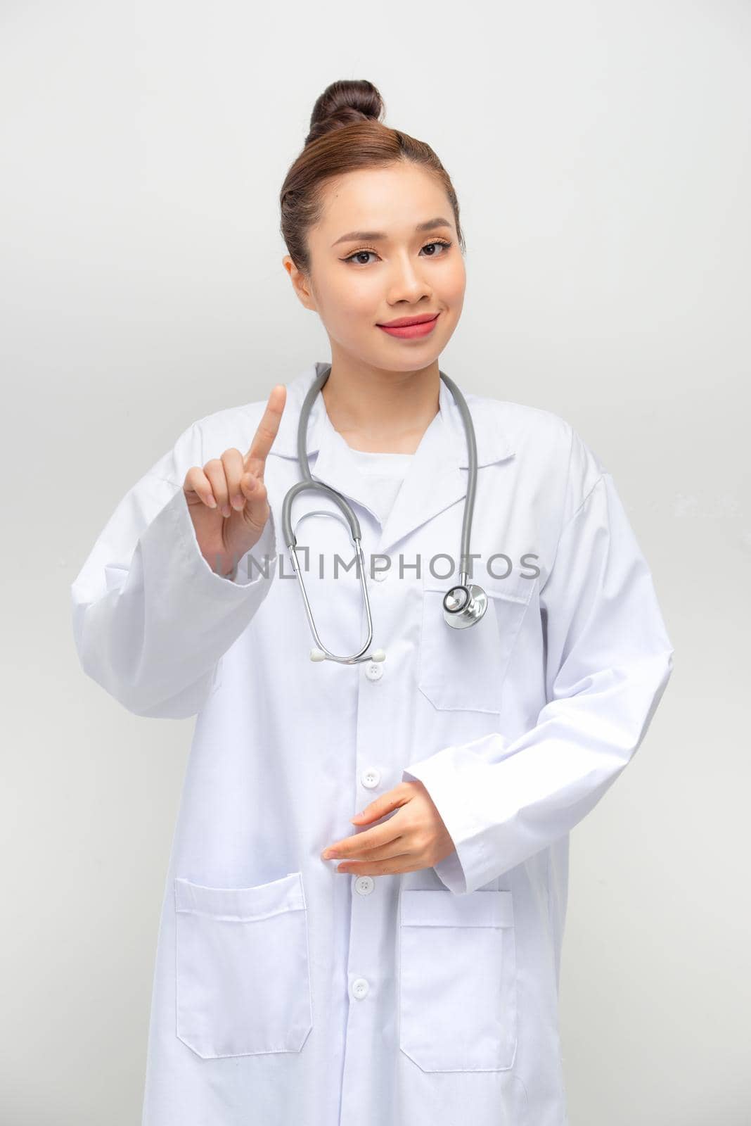 Young beautiful woman doctor in a white coat shows a sign with finger attention on white background.