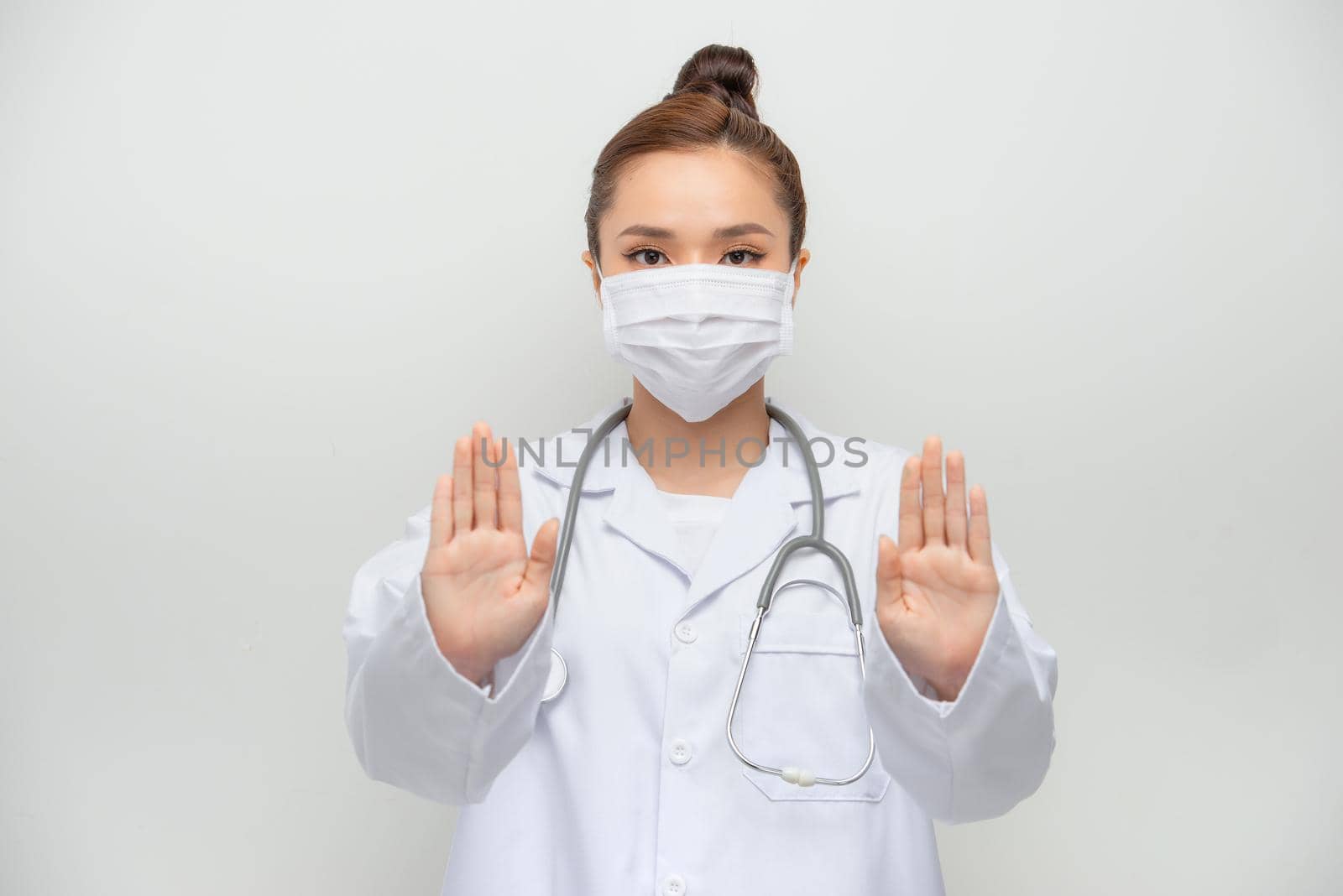 Serious-looking asian female doctor in medical mask, white coat make stop, cross sign, forbid coming outside by makidotvn