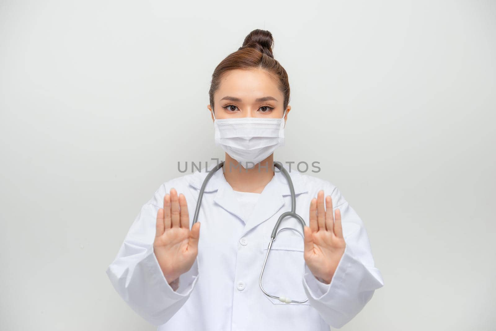 A young beautiful woman doctor in a white coat shows a stop gesture on white background. Say No virus disease.