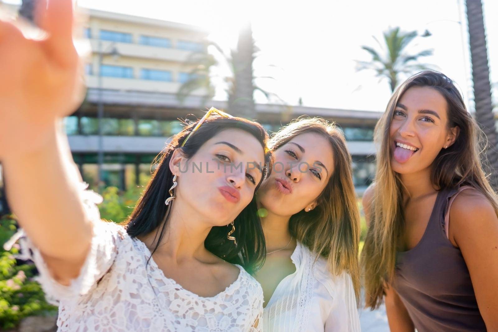 Three beautiful, funny playful girls have fun on vacation taking self portrait with smartphone making cheeky face . Carefree youth generation spending time on social network sharing picture and video by robbyfontanesi