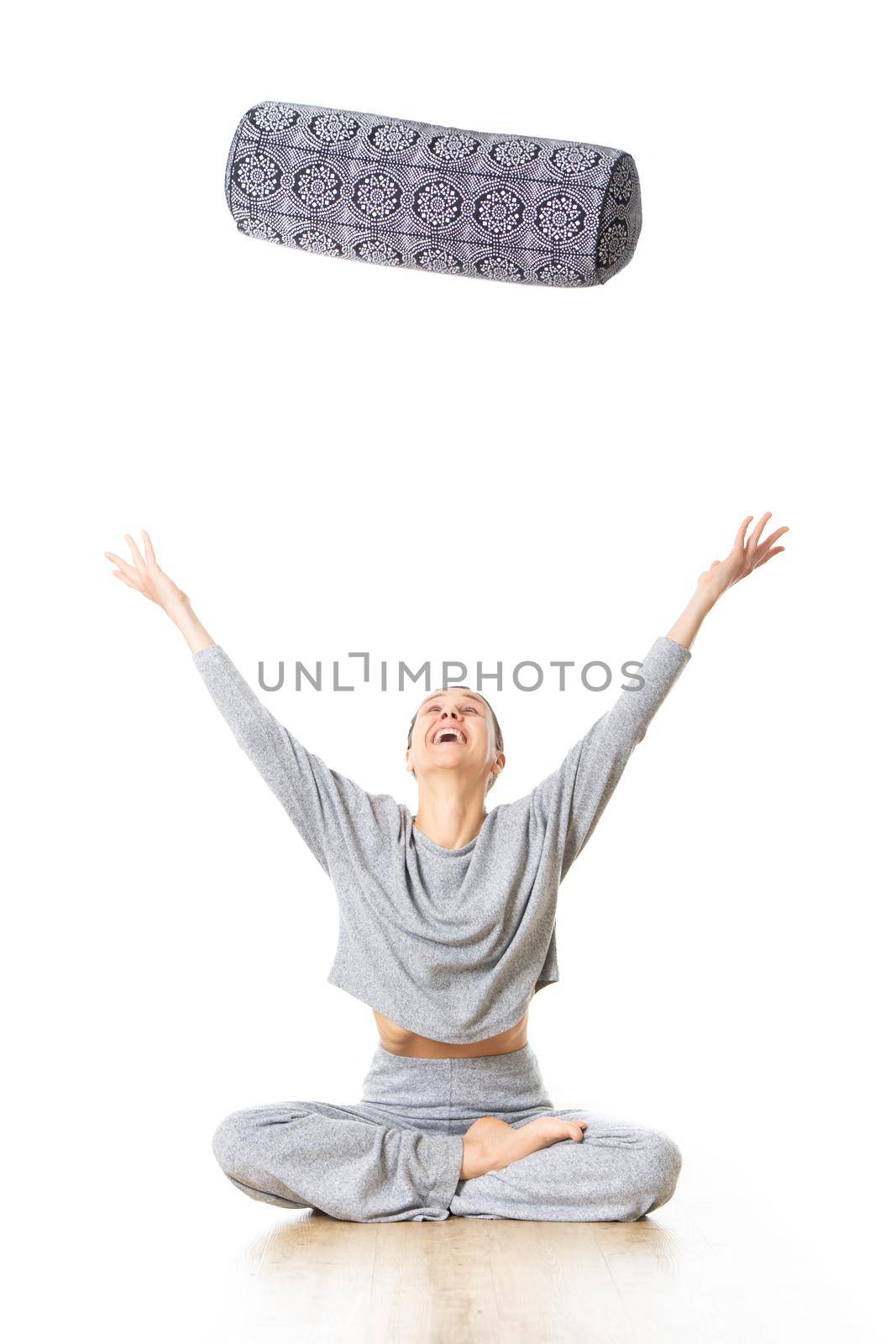 Restorative yoga with a bolster. Young sporty female yoga instructor in bright white yoga studio, throwing bolster cushion in air , smilling, showing love and passion for restorative yoga.