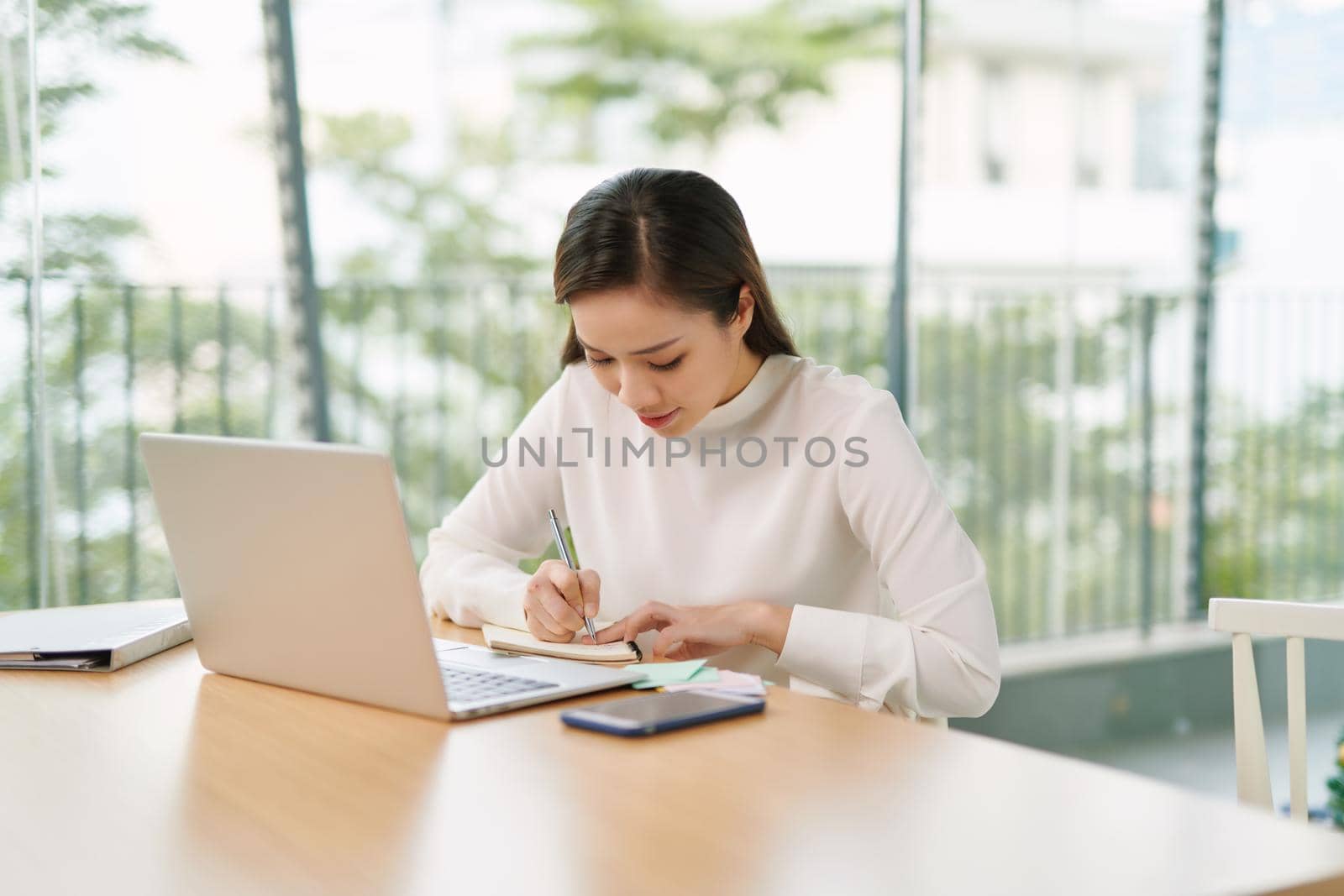 Young business woman sitting at table with notebook in room by makidotvn
