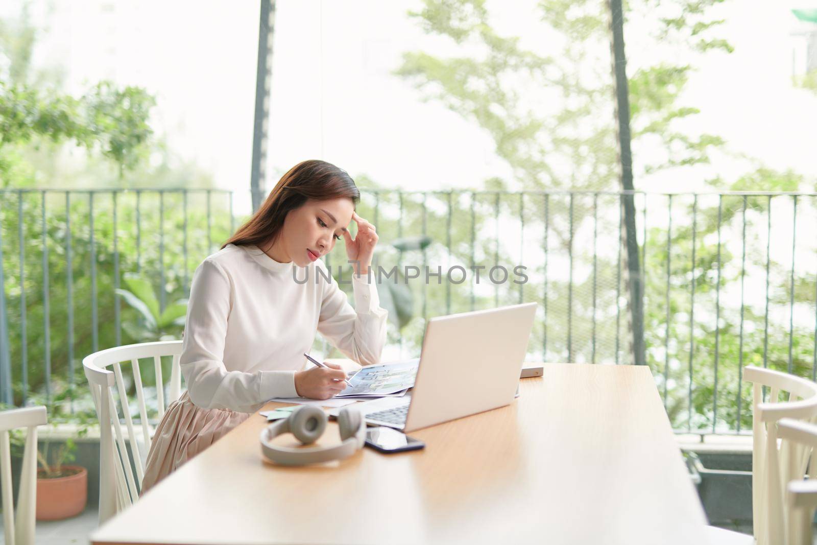 Portrait of beautiful confident woman is sitting at the table in front of computer and checking information in her diary and on the internet