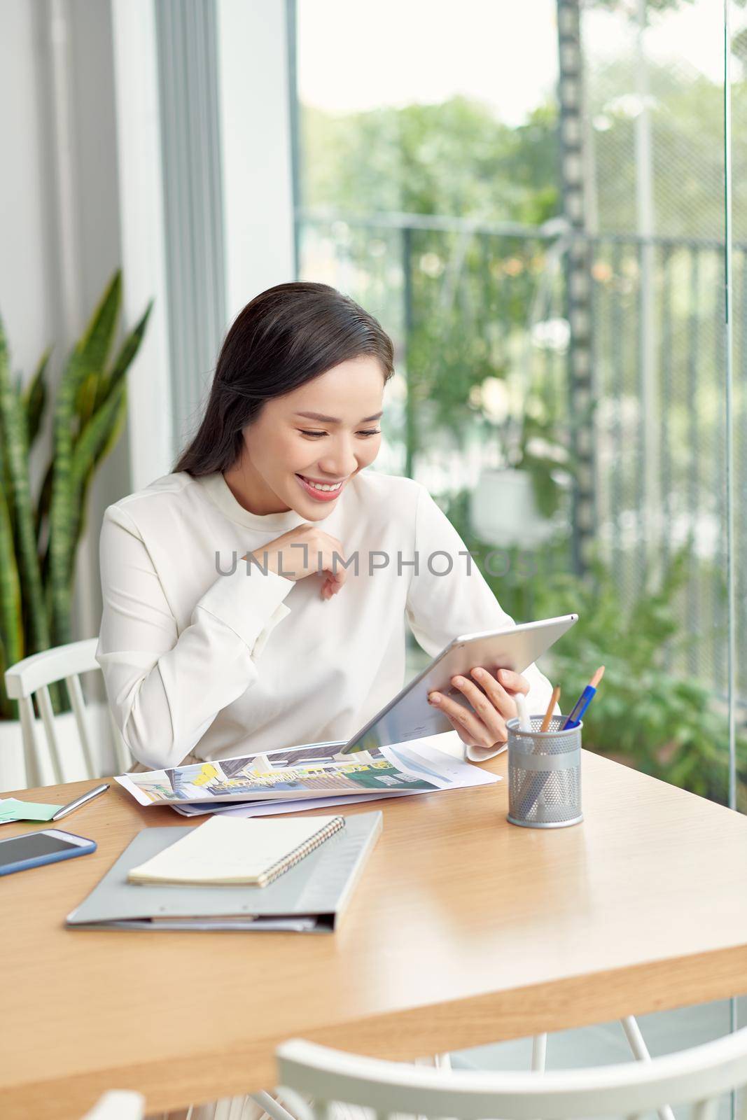 Happy young Asian woman sitting at table in her dining room making notes, selective focus by makidotvn