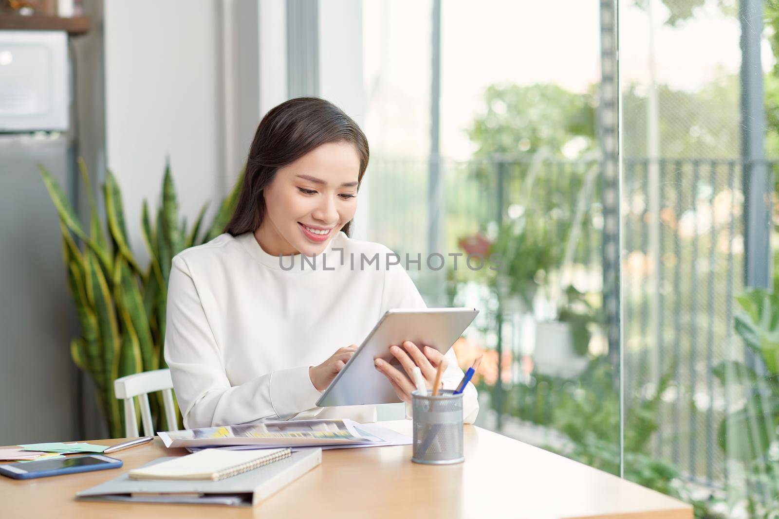 Young asian woman using smartphone while sitting at her office desk in modern office. by makidotvn