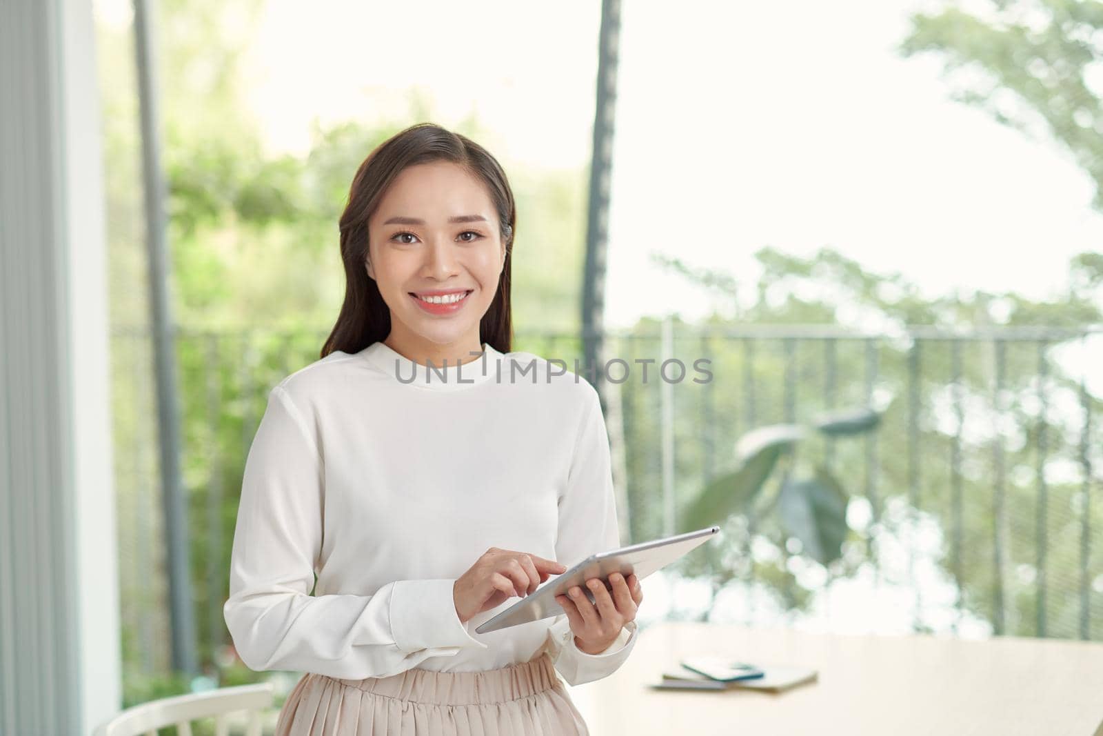 Attractive businesswoman using a digital tablet while standing in front of windows in an office building by makidotvn