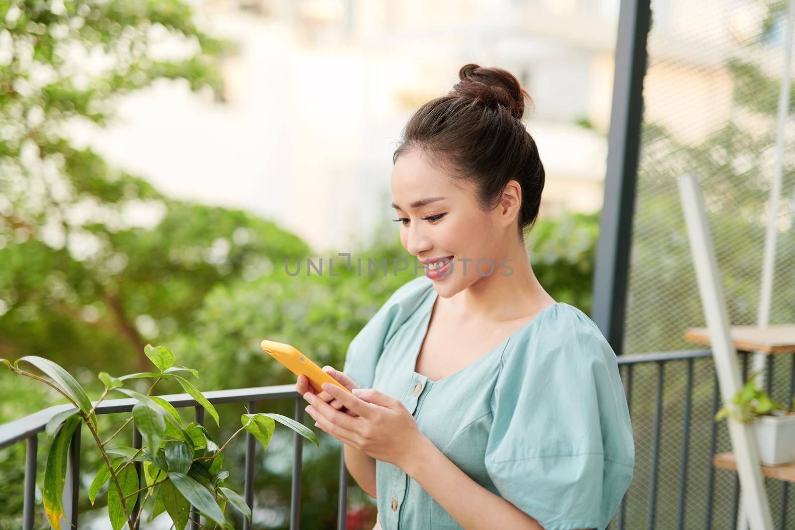 Young Asian woman enjoying nature and using phone on the balcony