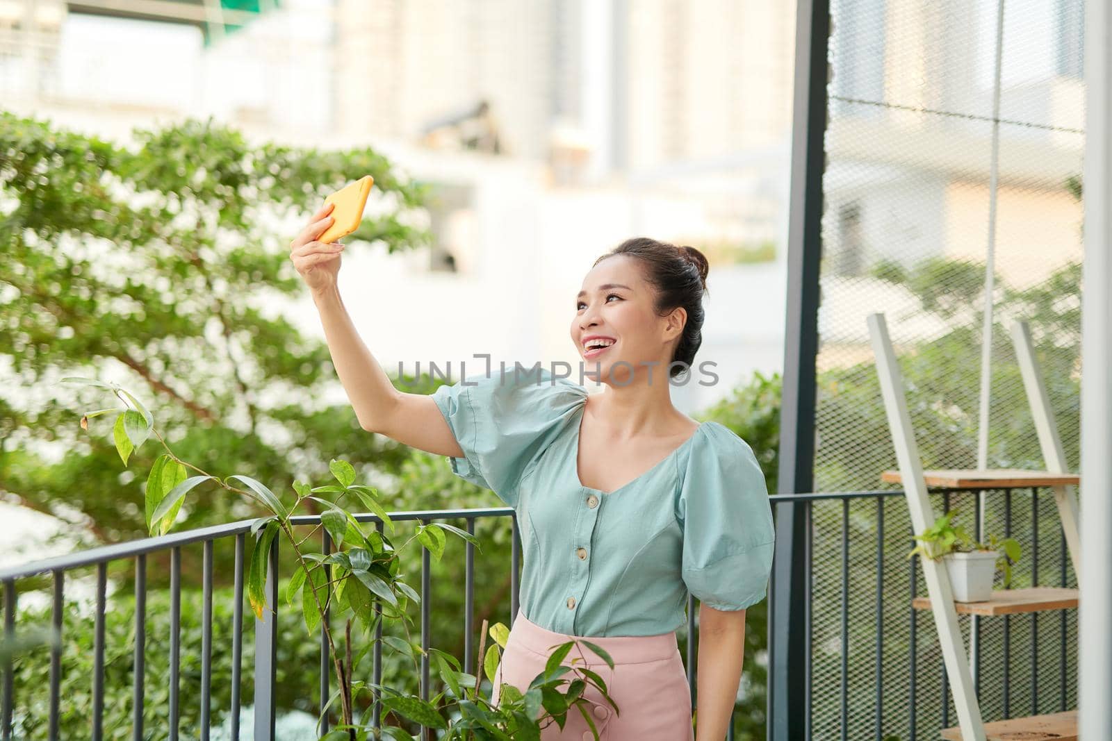 Cheerful young Asian girl having a video call with her phone when standing o balcony.