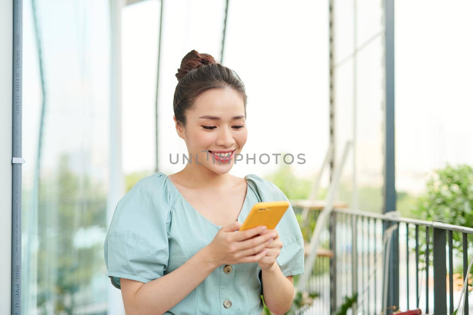 Beautiful young Asian woman holding phone and standing on the balcony.