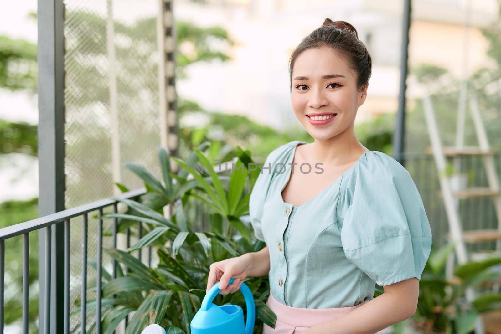 Happy Young Asian Woman housewife Watering flowers On Balcony.