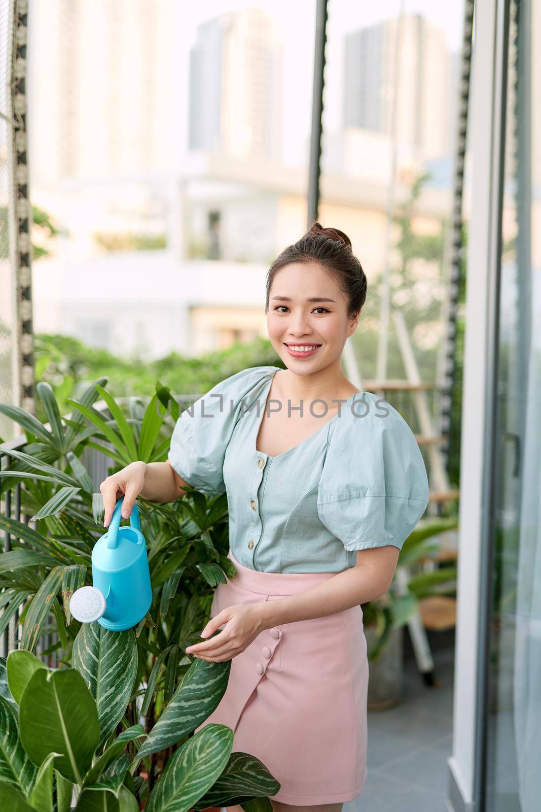 View of a Young woman watering the garden on her city balcony garden - Nature and ecology theme by makidotvn