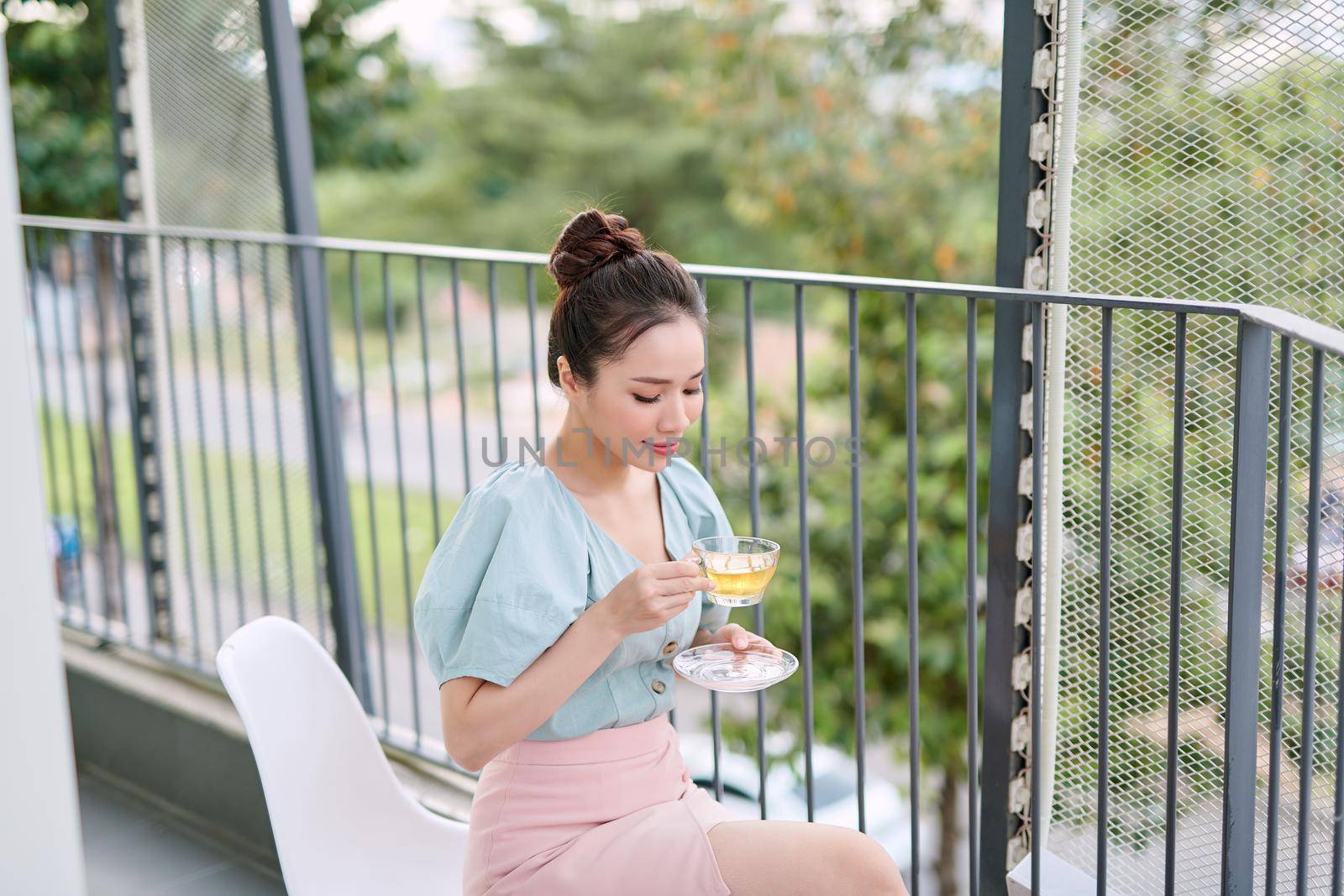 Elegant young Asian woman drinking tea at the balcony. Relaxing, enjoying life. 