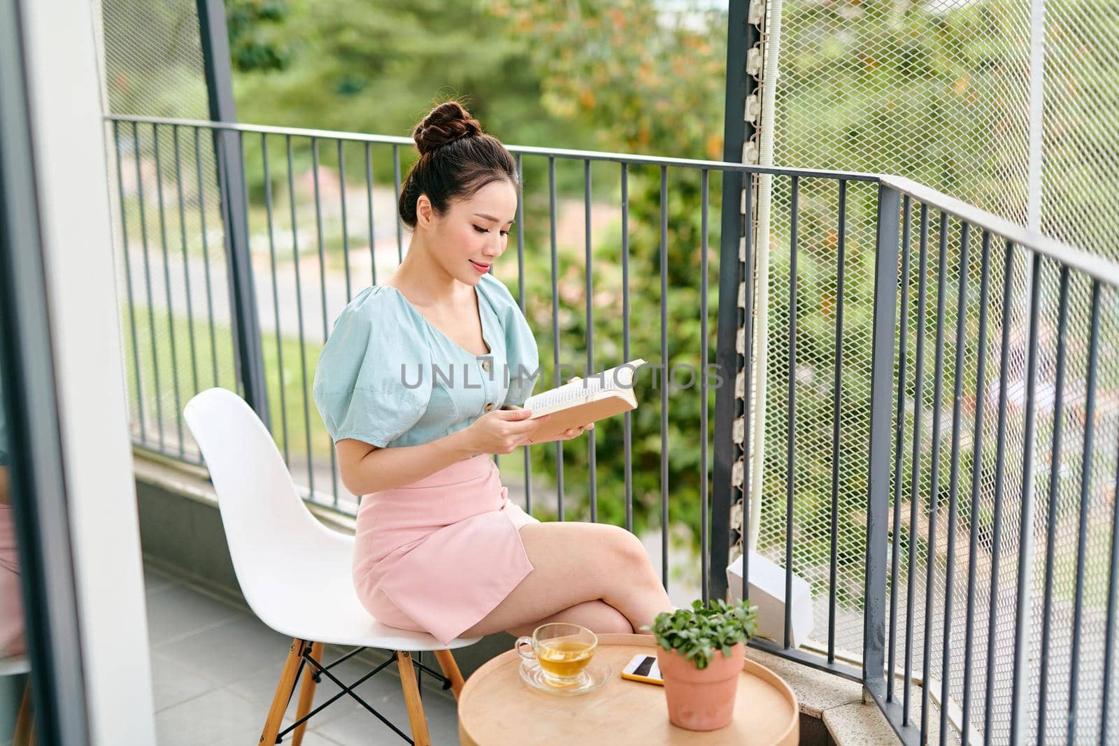 Young attractive Asian girl reading a book on balcony. by makidotvn