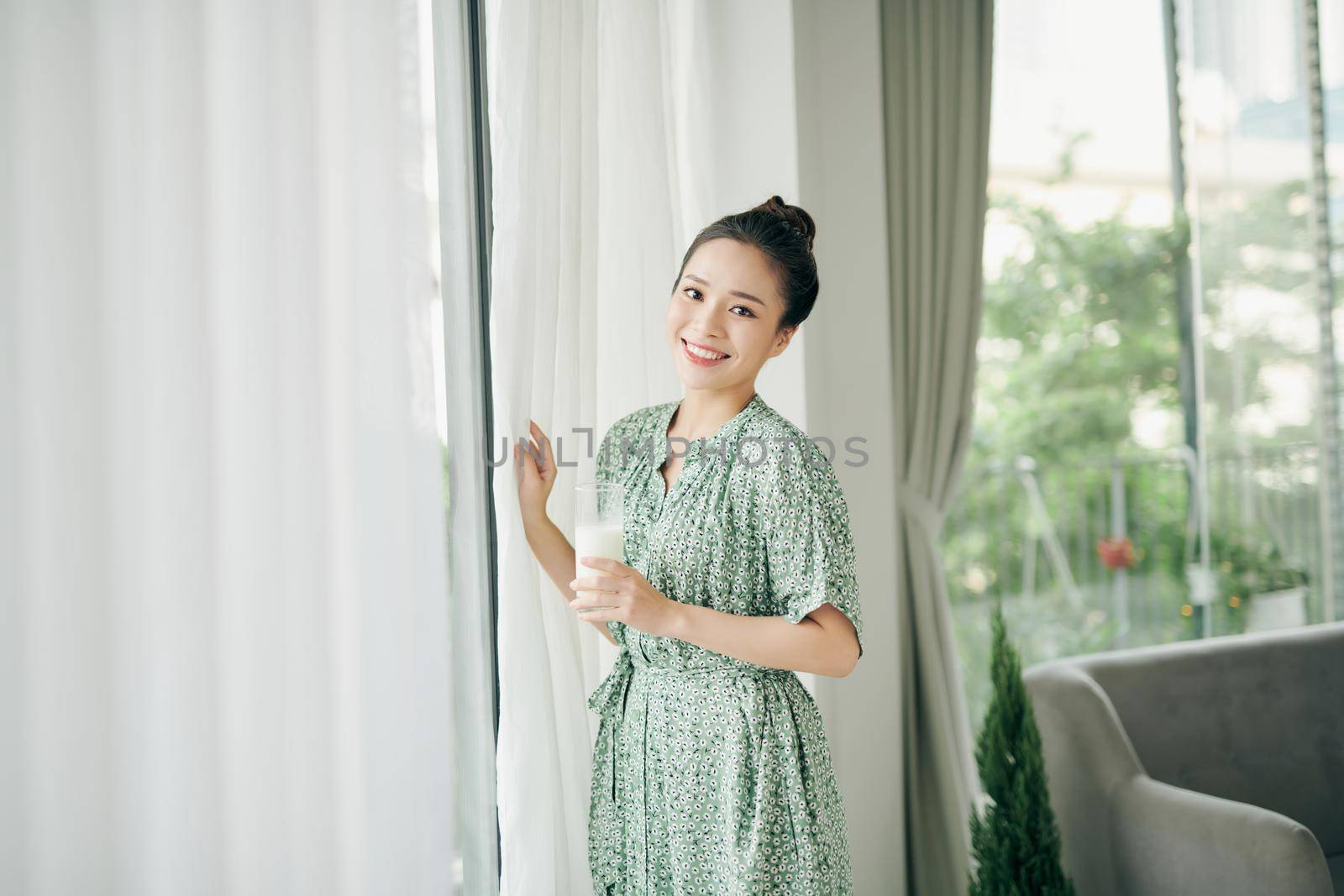 A young woman drinking milk at home near the window, healthy food eating.