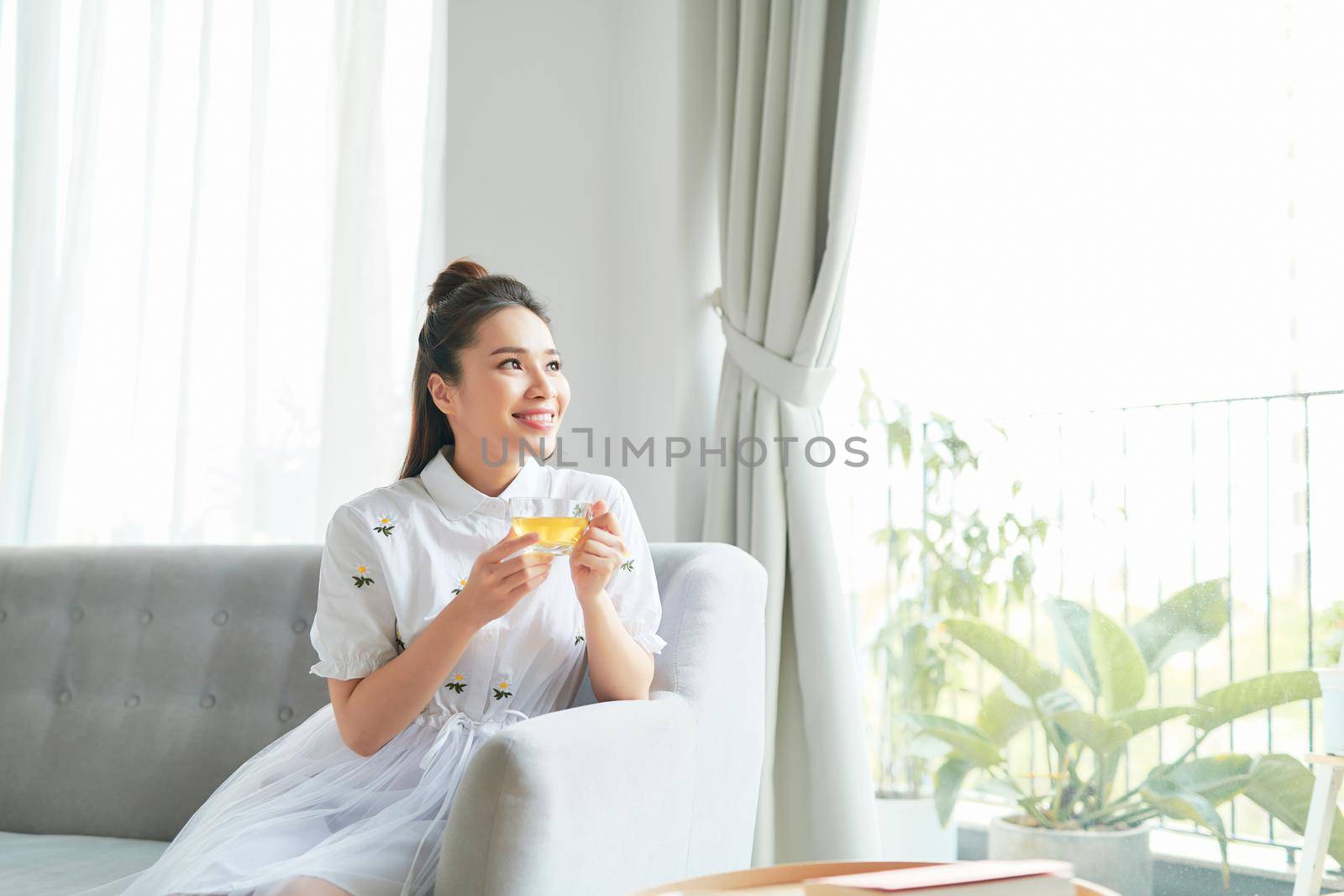 Positive young attractive woman in her room holding and enjoying a cup of tea by makidotvn