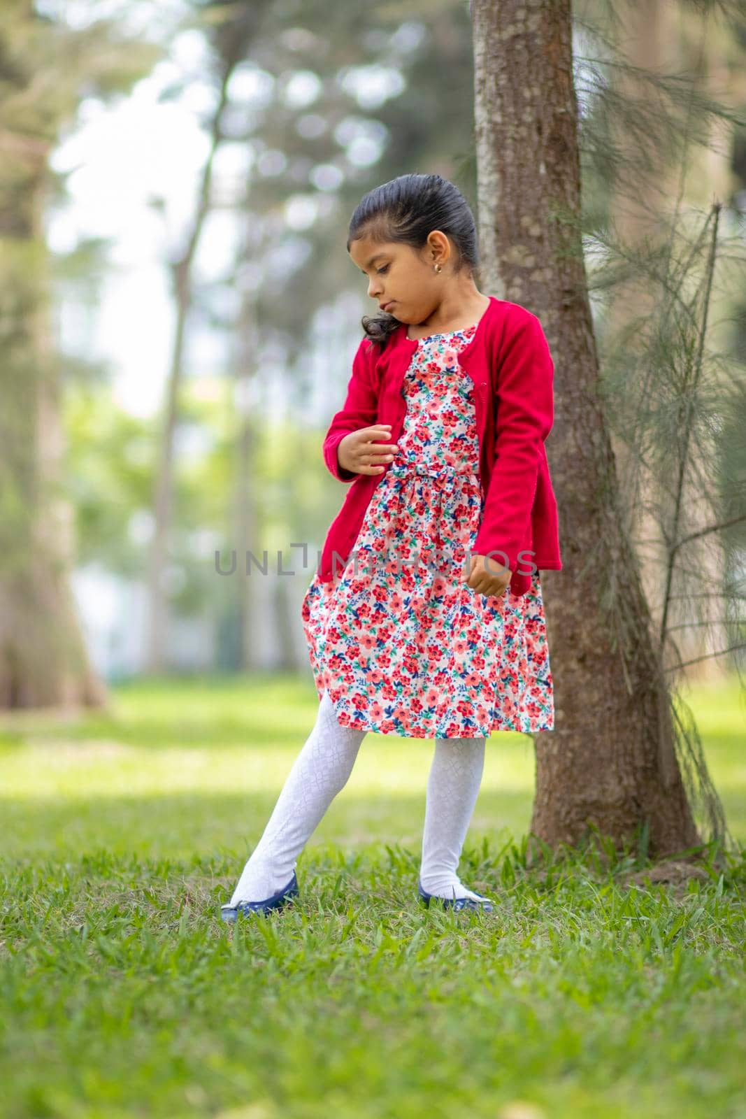 Little girl in flower dress and red sweater, very happy and smiling in the forest