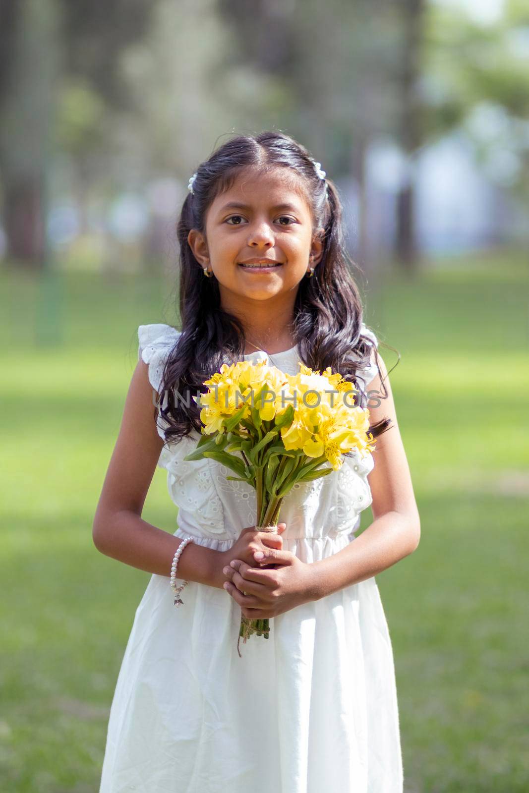 Little girl in white dress and with a cute bouquet of flowers in her hand