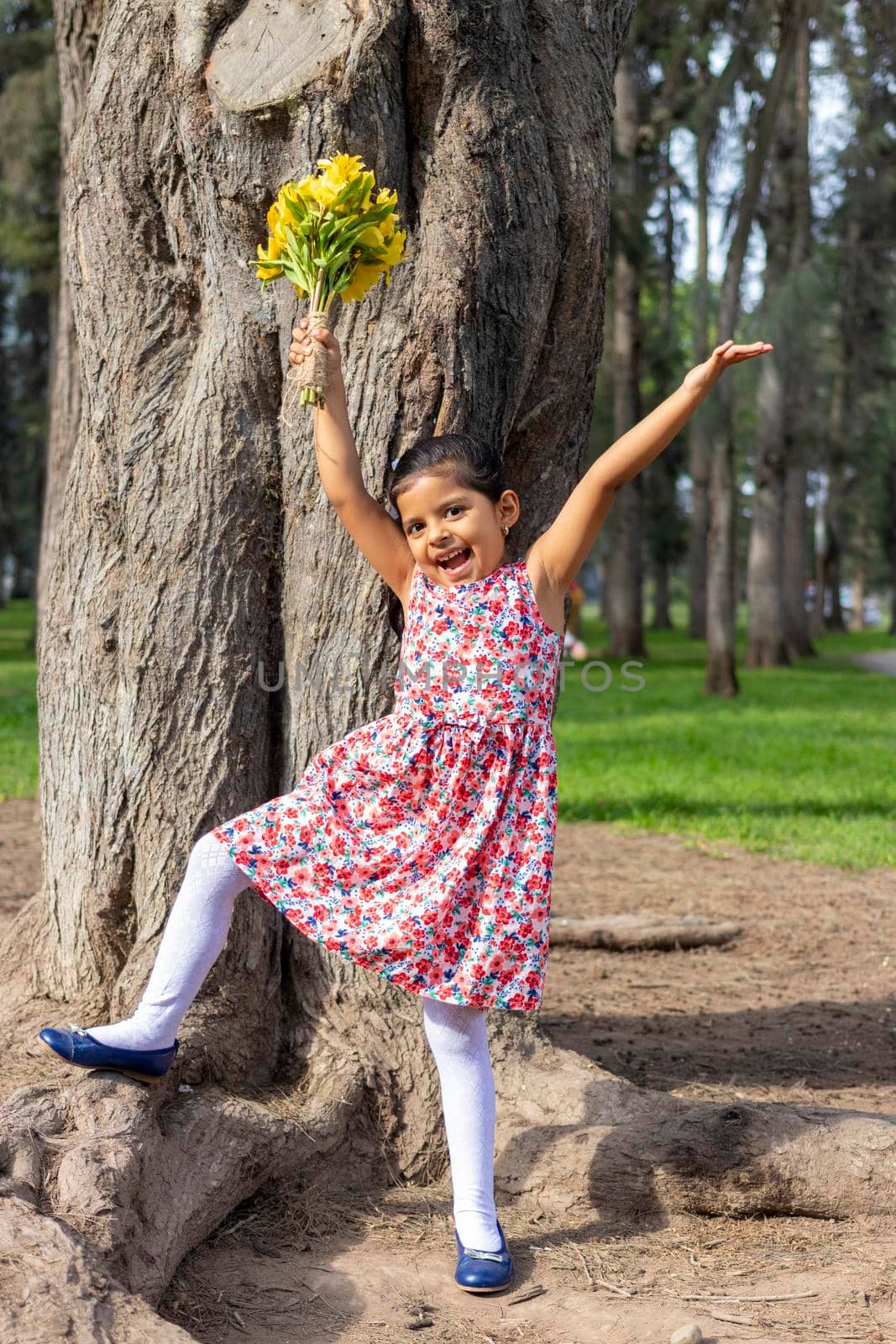 Little girl in dress celebrating in the park with a bouquet of flowers in her hand