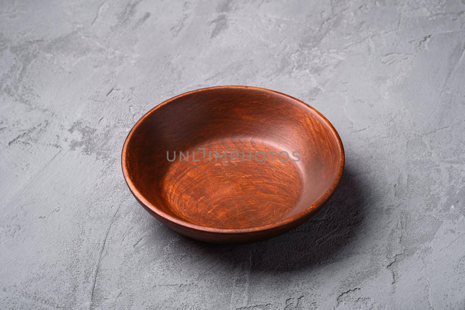 Empty round handcrafted brown wooden plate on stone concrete background, angle view by Frostroomhead