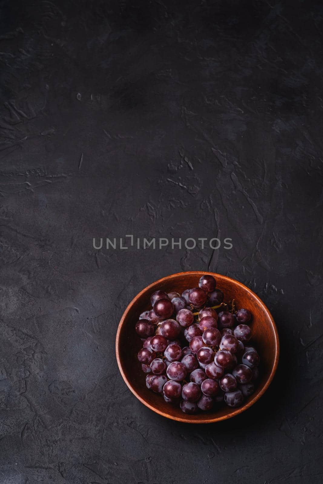 Fresh ripe grape berries in brown wooden bowl on dark stone background, angle view copy space
