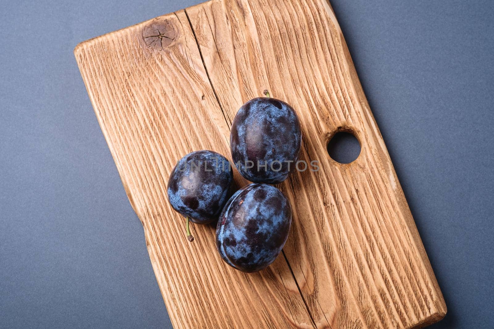 Fresh ripe plum fruits on wooden cutting board on blue grey minimal background, top view