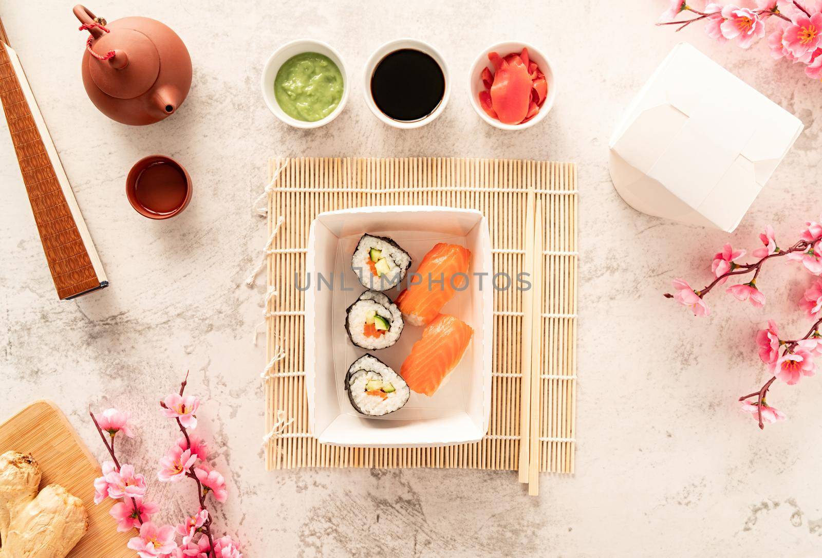 Japanese cuisine concept. Disposable tableware, zero waste packaging. Sushi set in disposable craft paper box with soy souce, ginger and wasabi. Teapot and chopsticks