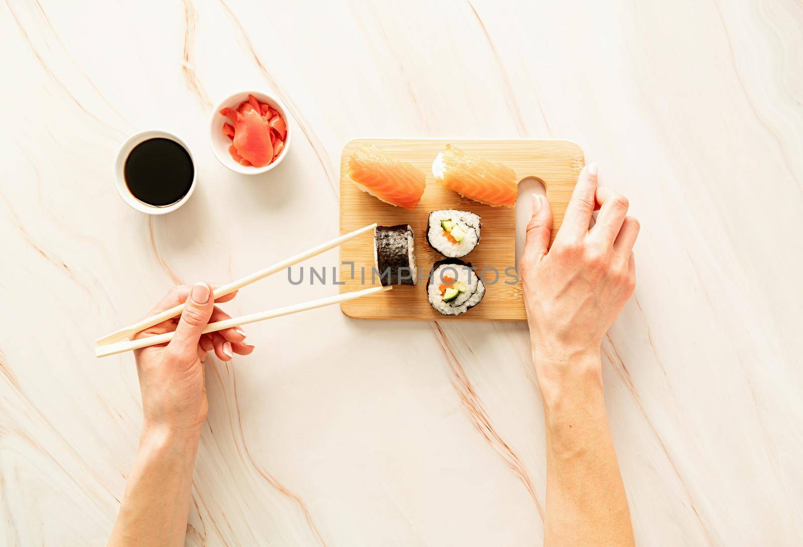 Japanese cuisine . Sushi salmon set on wooden cutting board. Woman hand holding sushi roll with chipsticks. Flat lay