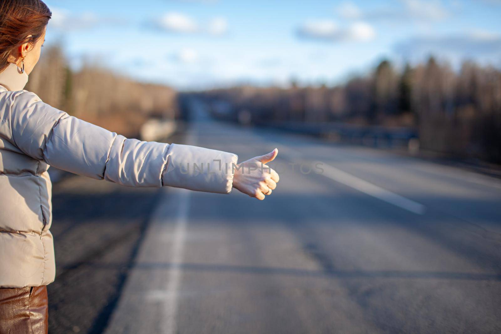 The girl stops the car on the highway with her hand. Stylish woman on the road stops the car go on a journey. A road in the middle of the forest.