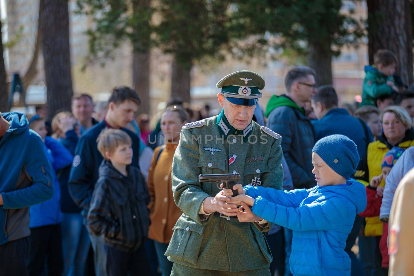 Reconstruction of the Second World War. A man in the uniform of a German officer shows a boy how to shoot a pistol. The Great Patriotic War. Liberation of Odessa. Zelenograd Russia April 18, 2021