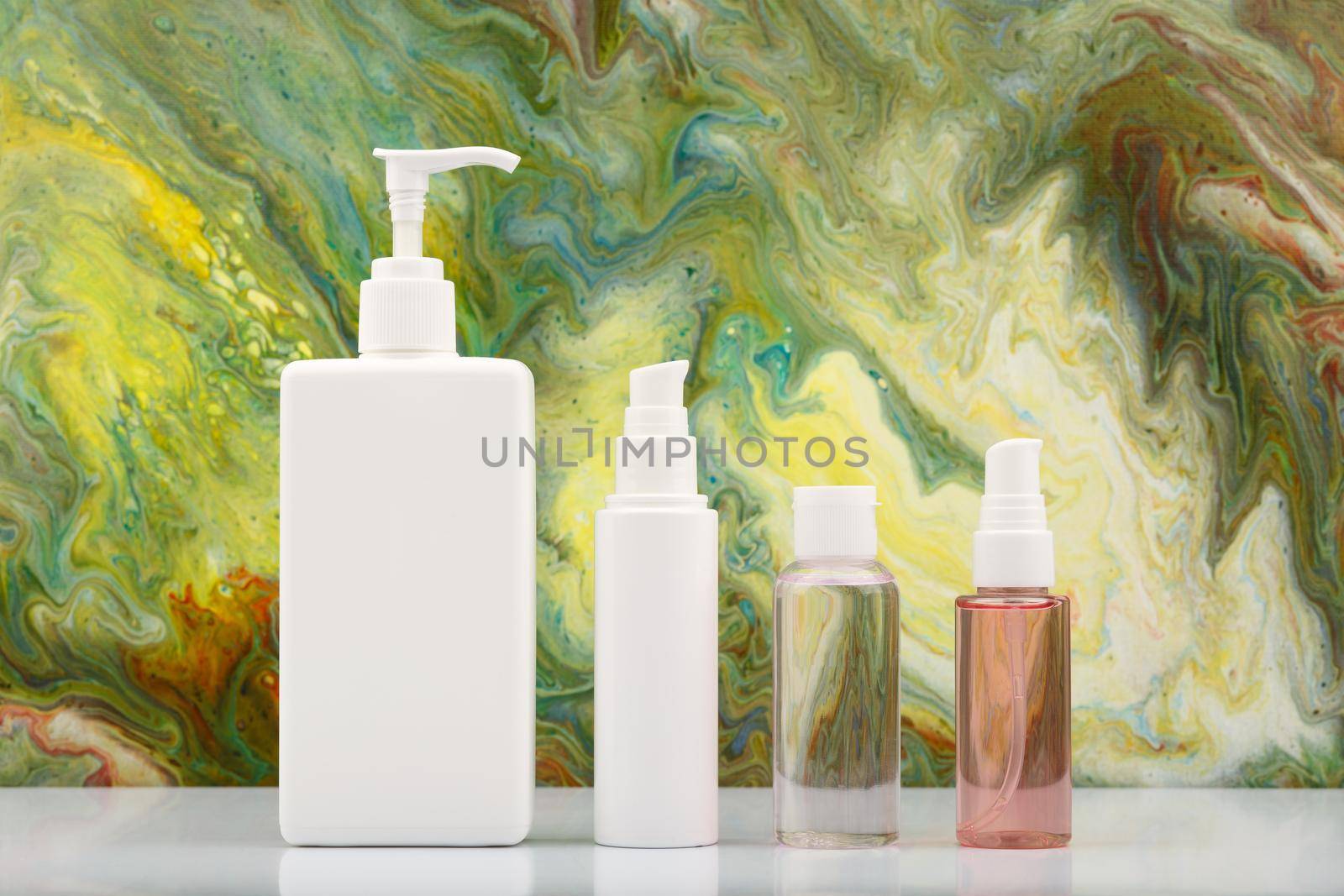 Set of skin care products against marbled background in green colors. Skin and body care concept. Body cream, face cream, exfoliating lotion and cleansing foam 