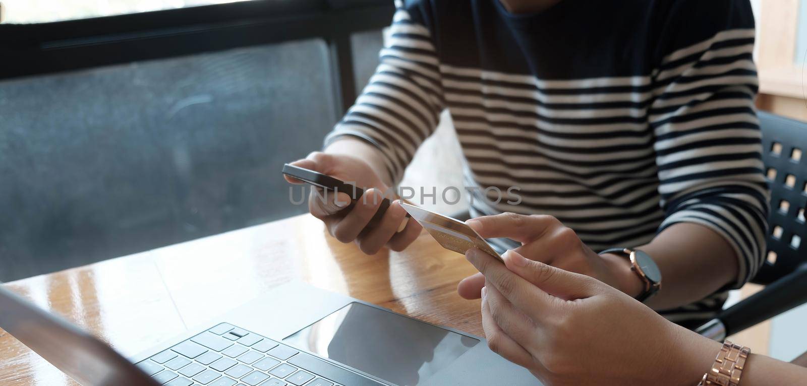 Two Asian women hold a credit card and use a smartphone to search for shopping information. by wichayada