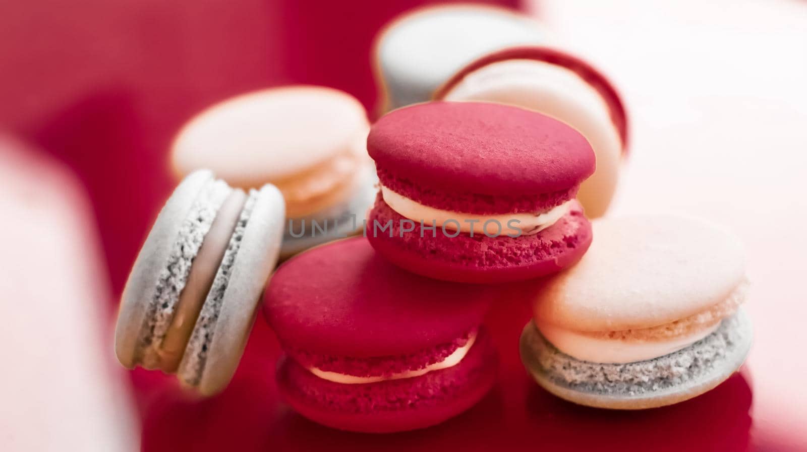 French macaroons on wine red background, parisian chic cafe dessert, sweet food and cake macaron for luxury confectionery brand, holiday backdrop design by Anneleven