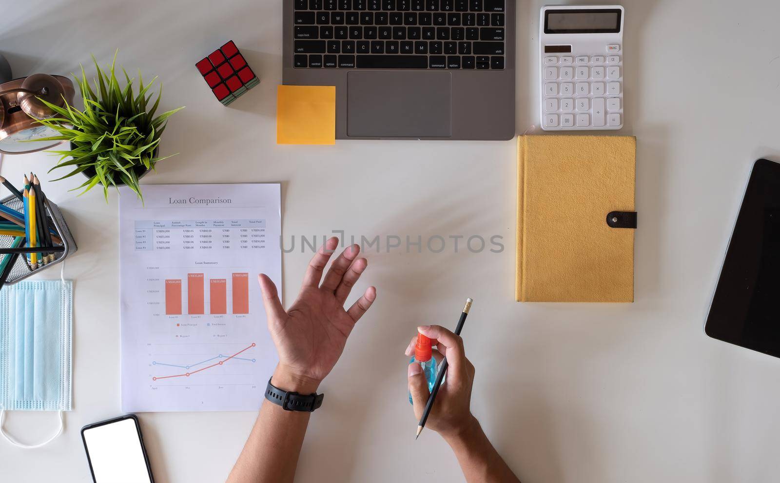 Above view of accountant man using alcohol spray for disinfecting hand washing against viral bacteria on workplace desk.