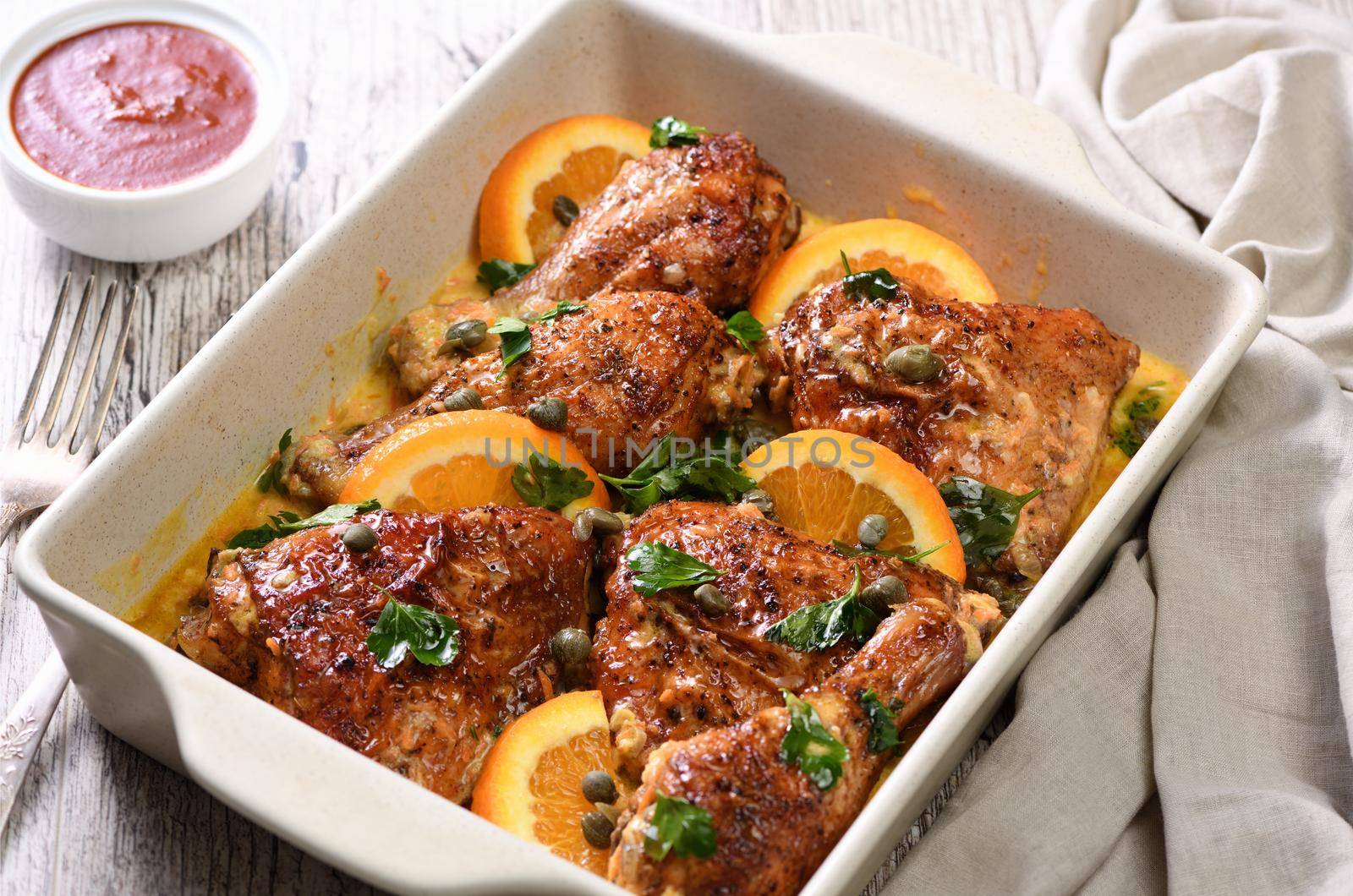 Slices of baked   chicken in a creamy sauce with oranges and capers in a baking dish