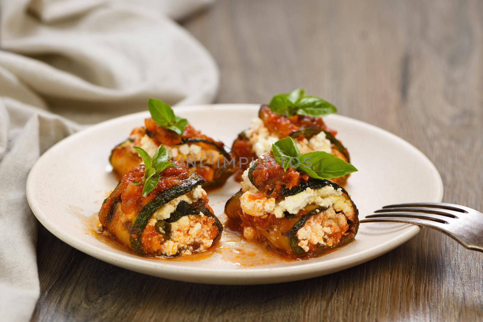 Baked zucchini rolls stuffed with ricotta and basil under tomato-onion-carrot gravy 