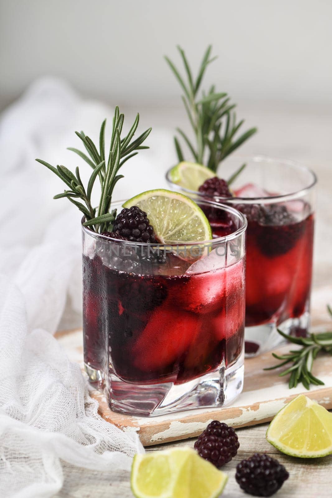 Two glasses of delicious refreshing lemonade with blackberry, ice and lime, decorated of rosemary. Cocktail on light table