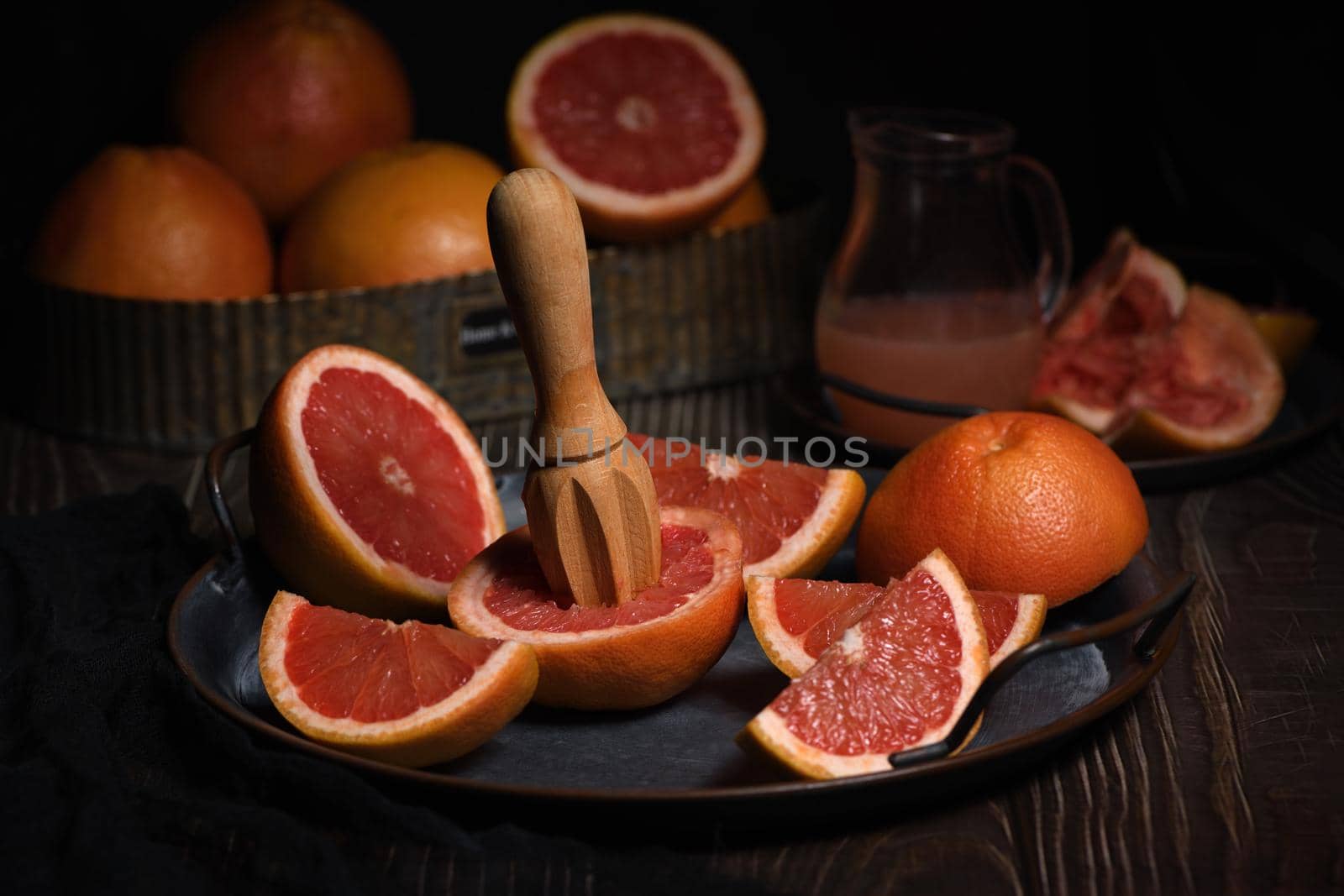 Slices of fresh grapefruit prepared for making fresh squeezed juice on a platter, dark background