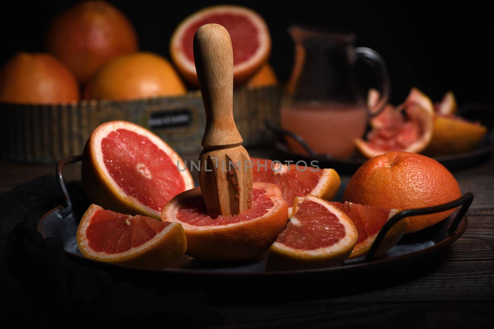 Slices of fresh grapefruit prepared for making fresh squeezed juice on a platter, dark background