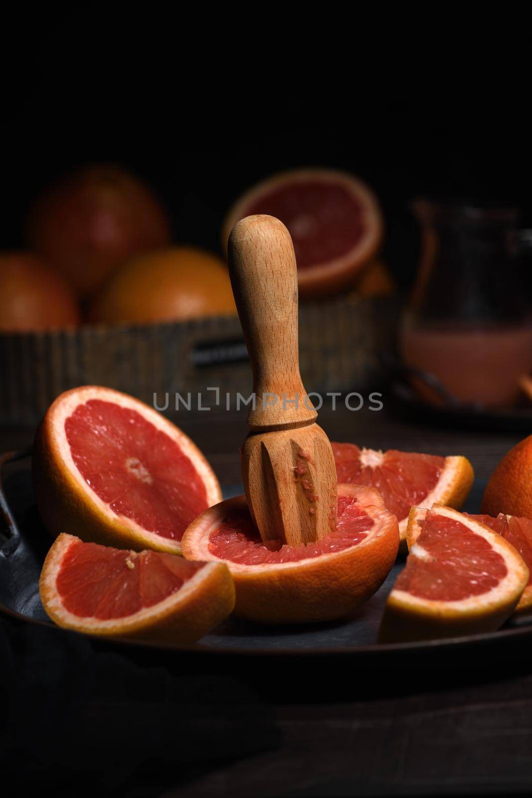 Slices of fresh grapefruit prepared for making fresh squeezed juice on a platter, dark background